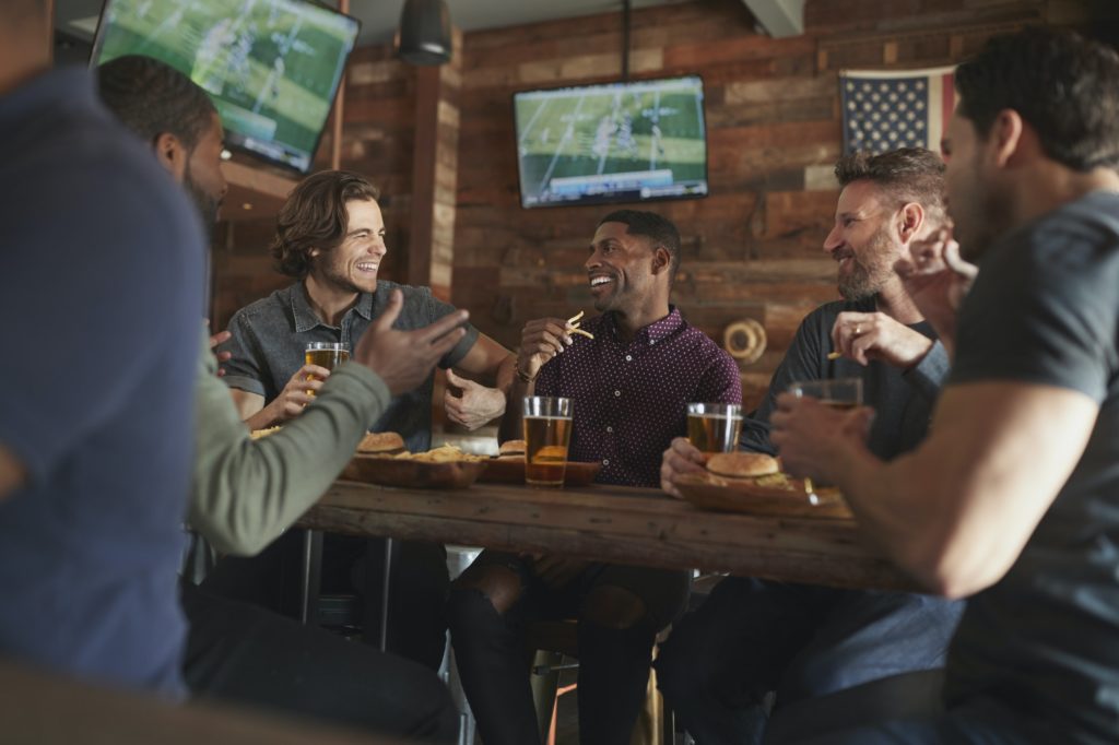 Male Friends Drinking Beer And Eating Burgers In Sports Bar